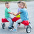 Three children smiling and riding the Simplay3 Boomerang Trike in a cul-de-sac
