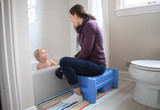 Mom sitting on the Periwinkle Sibling Step Stool during bath time